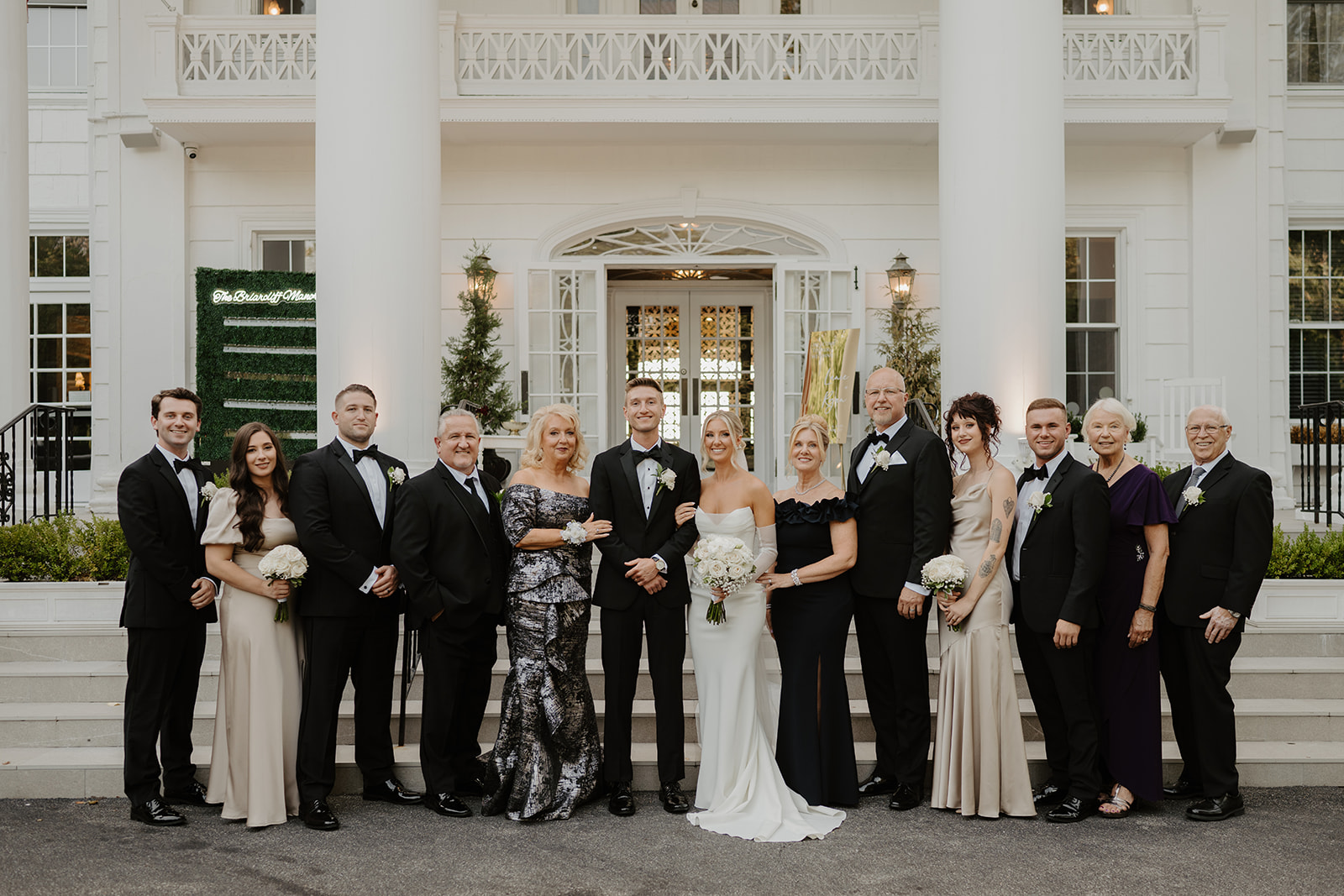 Newlyweds stand with their family for a wide formal group portrait on the steps of The Briarcliff Manor.